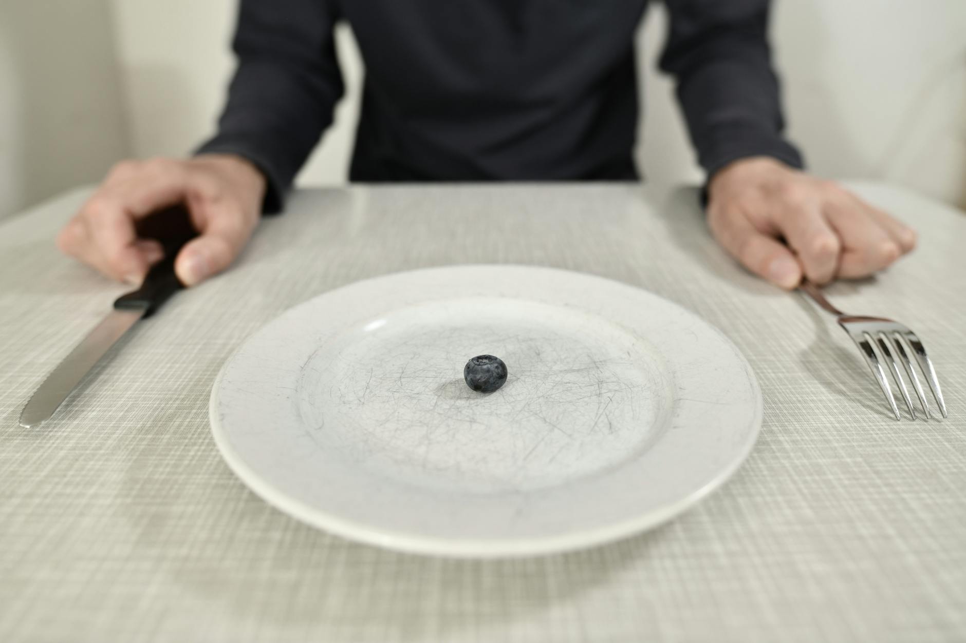 person sitting at table with one berry on plate